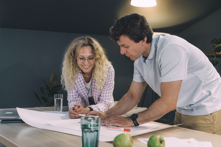 Two adults collaborating over blueprints, brainstorming ideas at a table.